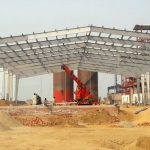Large pre-engineered steel building structure under construction, showing its framework on a wide industrial site.
