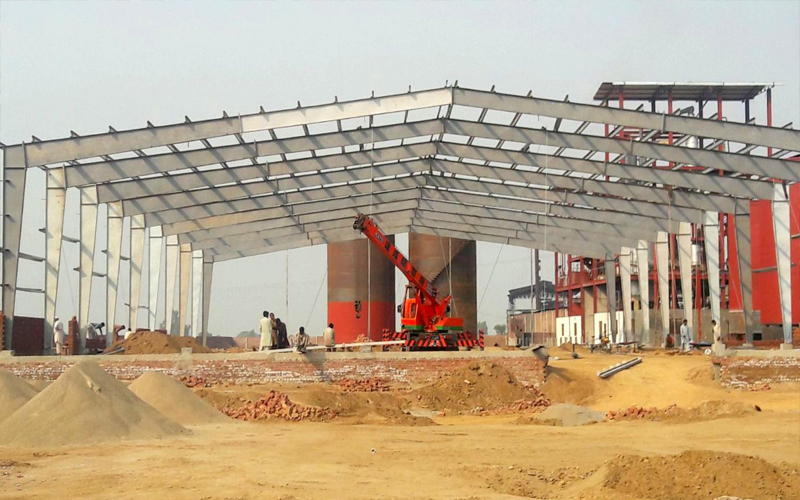 Large pre-engineered steel building structure under construction, showing its framework on a wide industrial site.